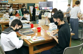 蔵書を点検し、汚れを拭き取る松阪工業高の大本君(手前右)ら=上川町の徳和小図書室で
